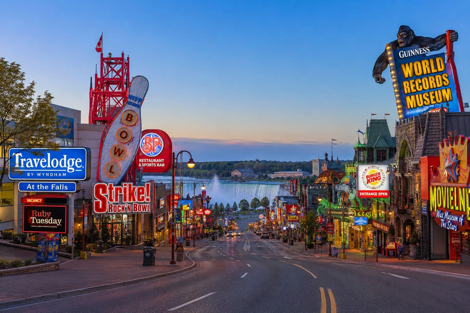 View down Clifton Hill at Niagara Falls toward the Niagara River with illuminated attraction signs on both sides of the street and Horseshoe Falls visible in the distance